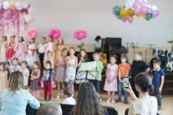 Παιδικό πάρτι στο δημοτικό σχολείο. Τα μικρά παιδιά στη σκηνή στο νηπιαγωγείο εμφανίζονται μπροστά στους γονείς. Θολή - Φωτογραφία, εικόνα