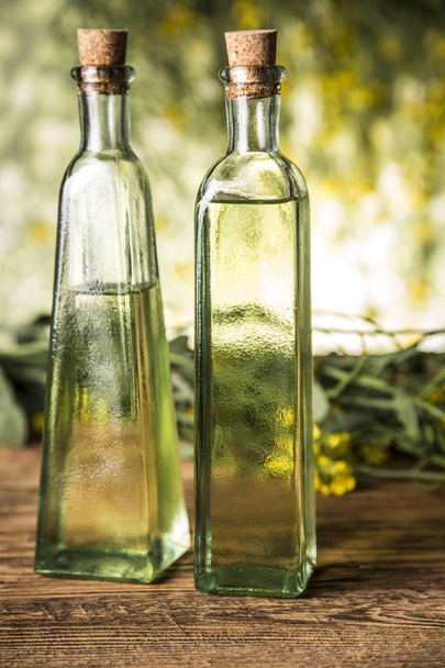 Rapeseed flowers and rapeseed oil in a bottle on the table - Фото, изображение
