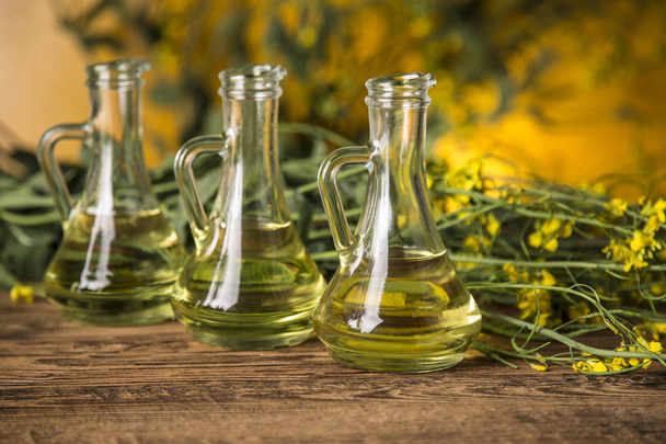Flores de colza y aceite de colza en una botella sobre la mesa - Foto, imagen