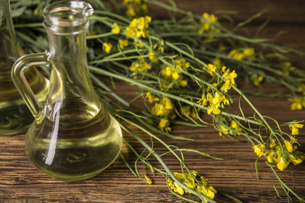 Rapeseed flowers and rapeseed oil in a bottle on the table - Photo, image