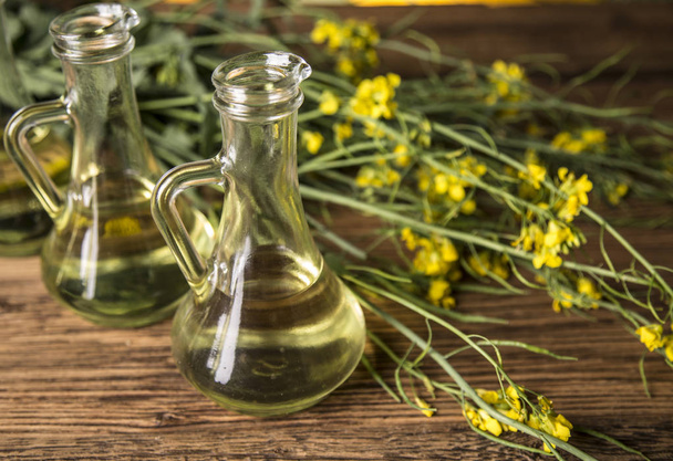 Rapeseed flowers and rapeseed oil in a bottle on the table - Foto, afbeelding