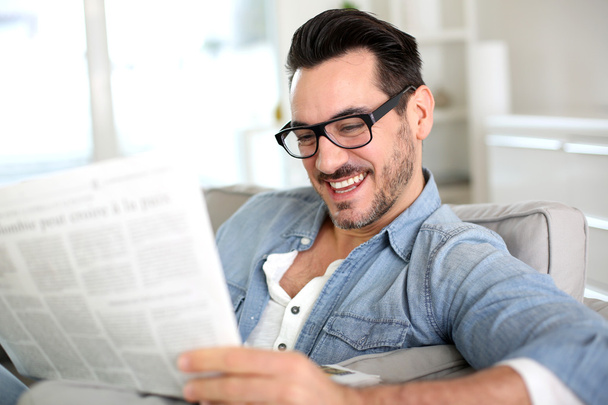 Cheerful guy reading newspaper in sofa - Фото, зображення