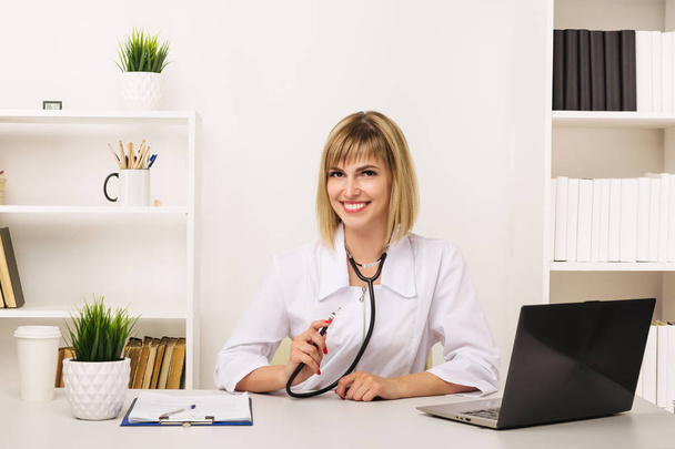 Přátelský ženský doktor pracuje u svého stolu v kanceláři - Fotografie, Obrázek