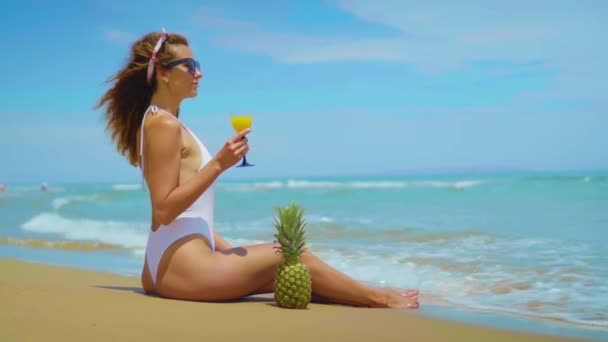 Веселая красивая молодая девушка сидит на пляже у моря с ананасом и соком
. - Кадры, видео
