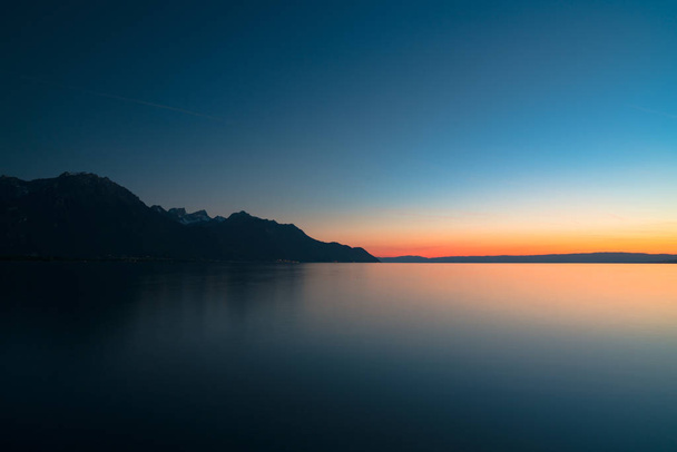 όμορφη μακρά έκθεση ηλιοβασίλεμα πάνω από μια ήρεμη λίμνη με το βουνό si - Φωτογραφία, εικόνα