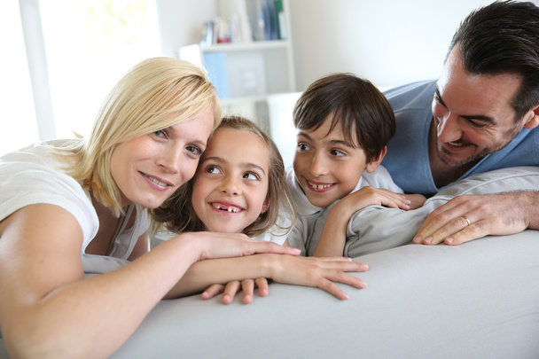 Neljän hengen perhe istuu sohvalla kotona
 - Valokuva, kuva