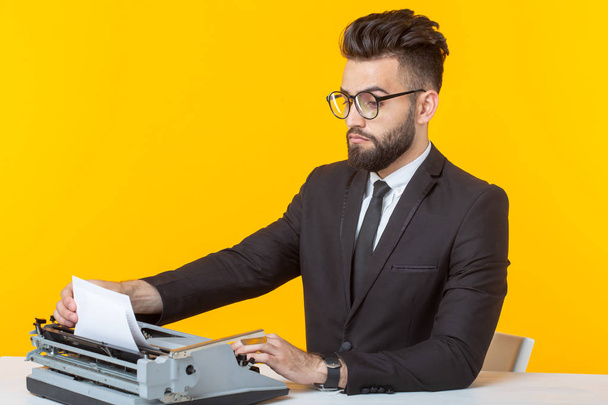 Widok z boku młodego uroczego biznesmena w formalnym stroju i okularach wpisując tekst na maszynie do pisania. Koncepcja spraw biznesowych i pomysłów. - Zdjęcie, obraz