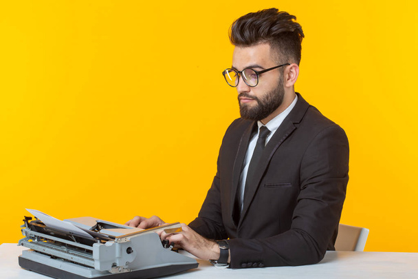 Young handsome male businessman in formal clothes typing text on a typewriter posing on a yellow background. Place for advertising. Business concept. - Foto, imagen