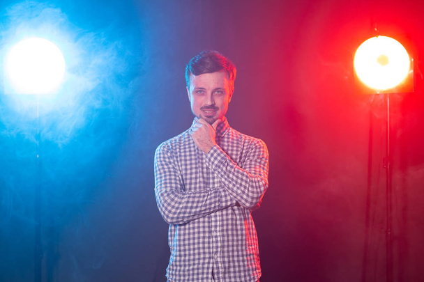 Encantador joven hipster sonriente hombre está posando sobre el fondo de la iluminación del estudio rojo y azul. Concepto de hombre pensativo
. - Foto, Imagen
