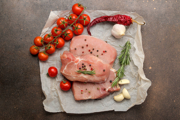 Rauwe varkensvlees steak, vlees en ingrediënten voor koken, specerijen, kruiden en groenten op een donkere achtergrond. Top View. - Foto, afbeelding
