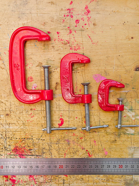 Set aus drei roten Metall-C-Klemmen und Lineal auf Holzboden - Foto, Bild