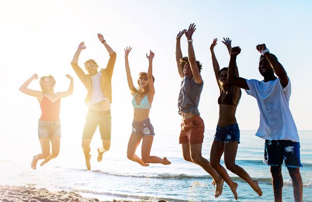 Happy lachende vrienden springen op het strand - Foto, afbeelding