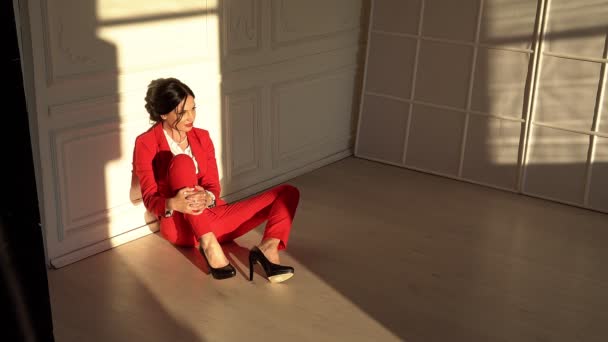 赤いスーツの魅力的なブルネットはスタジオに座ります - 映像、動画