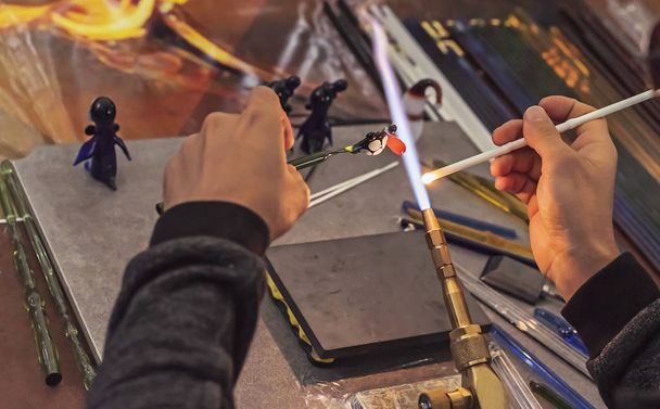 Glassblower makes a figurine of glass. Melting glass on a gas burner. - Photo, Image