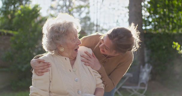 Granddaughter visiting,happy hugging grandmother at outside garden,backlight sun. Multigeneration women love holding together.White hair elderly grandma woman.Affection,togetherness,caring,loving - Footage, Video