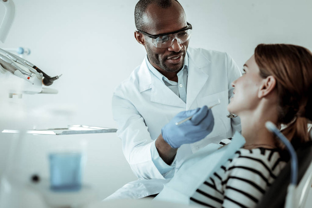 konzentrierter dunkelhäutiger Arzt, der seine Patientenzähne heilt - Foto, Bild