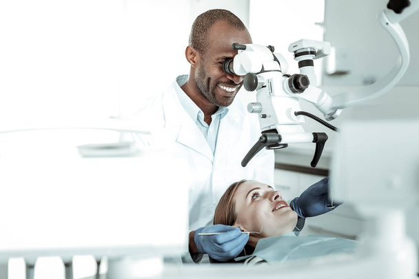 Dark-skinned doctor wearing uniform and looking in special microscope - Foto, afbeelding
