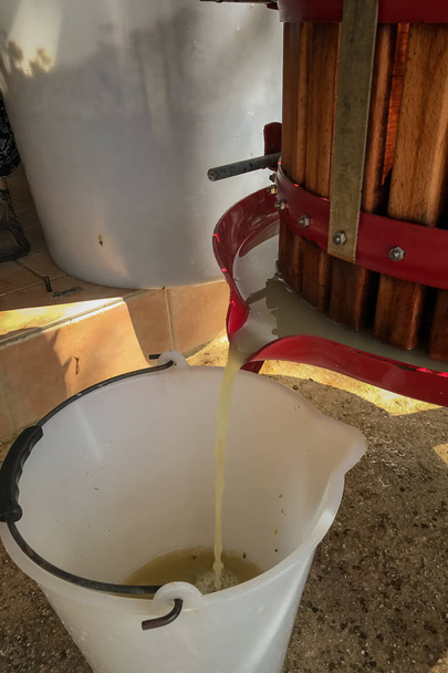 A close up of an old fashioned wooden barrel shaped grape press with the juice from the pressed grapes running into a white bucket - Photo, Image