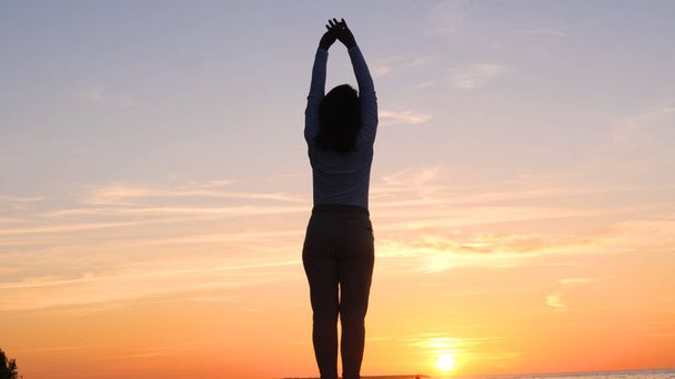 Młoda kobieta na tle zachodu słońca słońce na wybrzeżu robi ćwiczenia wykonywane przez bieganie, rozciąganie i opadanie, Dziewczyna na morzu uprawia jogę. Portret: Wolny ruch, Zachód słońca. - Zdjęcie, obraz