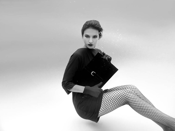 monochrome beautiful amazing stylish pretty young woman in green dress, red gloves, black clutch bag and tights in the net underwater in the swimming pool. Fashion concept - Фото, зображення