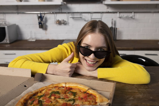 Zabawna brunetka dziewczyna w żółtym swetrze i czarne okulary jedzenia; p - Zdjęcie, obraz