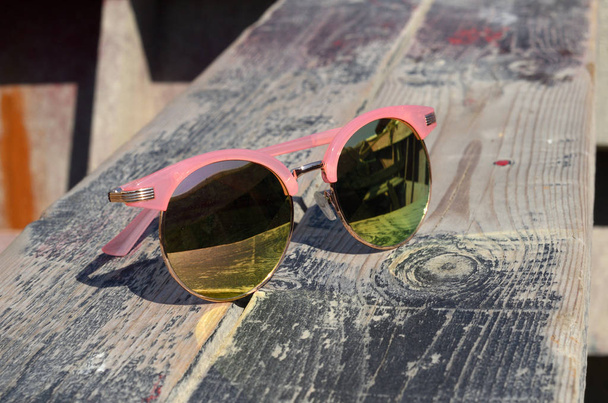Pink napszemüveg a nap ellen egy fából készült háttér közelében  - Fotó, kép