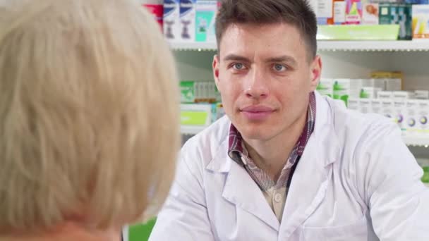 Male chemist listening to his senior female customer request on medicine - Footage, Video