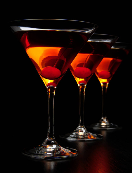 Group of three manhattan drinks in bar with cherry on black - Fotó, kép