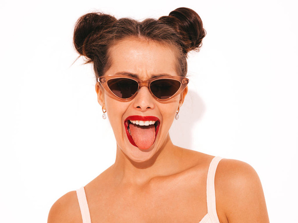 Young beautiful sexy smiling hipster woman with red lips in sunglasses.Trendy girl in summer swimwear bathing suit. Positive female going crazy.Funny model isolated on white.Shows tongue.Two horns - Фото, изображение