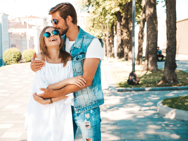 Smiling beautiful girl and her handsome boyfriend. Woman in casual summer dress and man in jeans clothes. Happy cheerful family. Female having fun on the street background.Hugging and kissing in head - Foto, Imagem