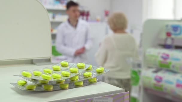 Pharmacist talking to senior client, pills blisters on foreground - Footage, Video