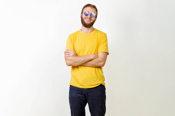 Portret młodego przystojnego mężczyzny w żółtej koszulce, okrągłe okulary przeciwsłoneczne i broda uśmiechnięty patrząc na kamerę na szarym tle. - Zdjęcie, obraz