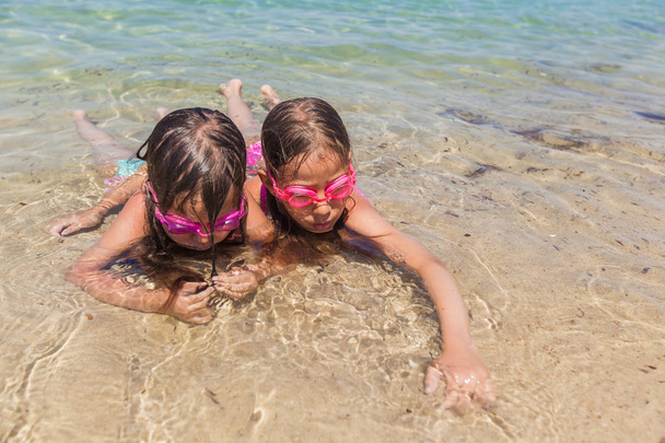Ευτυχισμένα μικρά κορίτσια που παίζουν στην αμμώδη παραλία στις καλοκαιρινές διακοπές - Φωτογραφία, εικόνα
