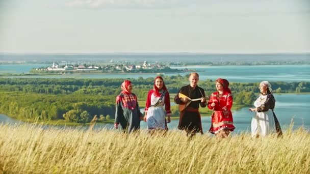 Lidé v tradičních ruských šatech, kteří chodí po hřišti a zpívají píseň-muž, který drží balalajka - Záběry, video