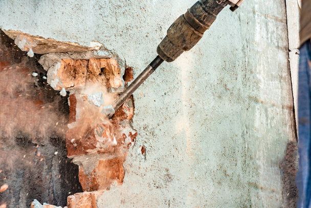 Demontage von Wänden und Öffnungen mit einem elektrischen Presslufthammer, Nahaufnahme, heiserer Staub unter dem Meißel. - Foto, Bild