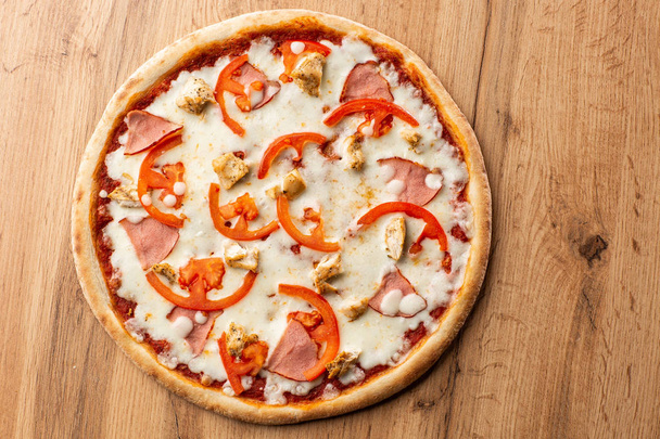 Flat Lay με παραδοσιακή ιταλική πίτσα με κοτόπουλο, ζαμπόν, τυρί και ντομάτες σε ξύλινη πλάτη. - Φωτογραφία, εικόνα