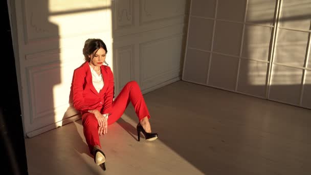 Ελκυστική μελαχρινή σε κόκκινο κοστούμι κάθεται στούντιο - Πλάνα, βίντεο