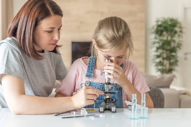 Mother and daughter make chemical experiments with microscope at home - Photo, Image