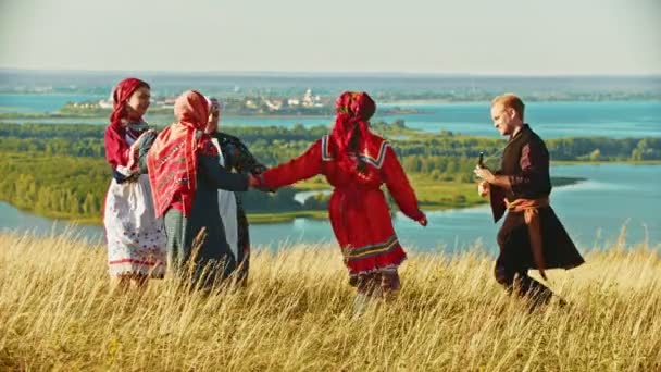 Mladý soubor v tradičních ruských šatech tančících na poli na pozadí řeky a ostrovů - Záběry, video