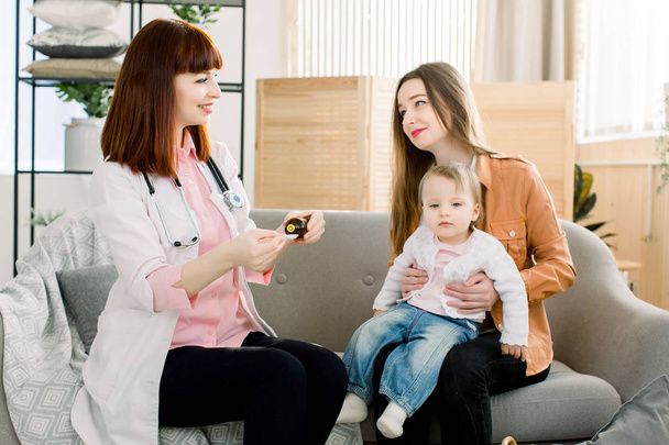 Young Caucasian woman doctor giving syrup medicine for little baby girl because of the flu, sick child and health care concept - Photo, Image