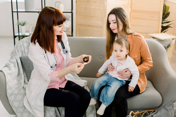 白いコートを着たホーム女性医師は、自宅や診療所で小さな赤ちゃんを検査します。親切な医師のセラピストは、咳シロップを与えるルックス - 写真・画像