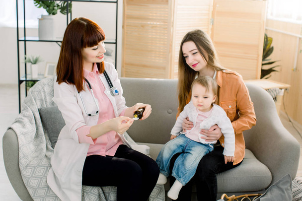 Young Caucasian woman doctor giving syrup medicine for little baby girl because of the flu, sick child and health care concept - Photo, Image