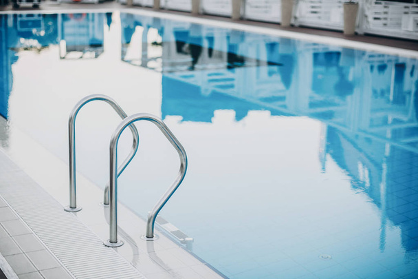 Stijlvol blauw zwembad met metalen ladder close-up bij modern hotel. Su - Foto, afbeelding