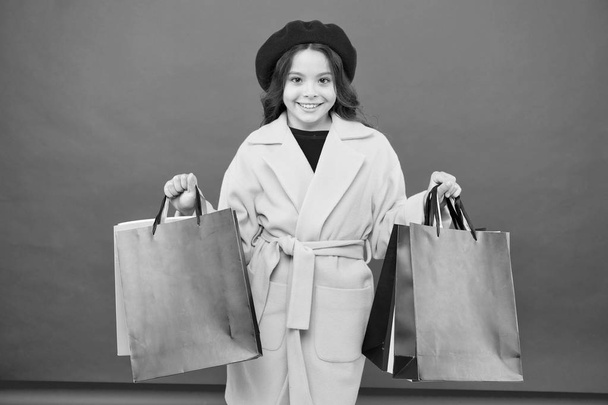 Fashionista zbožňují, nakupování. Posedlý nakupování. Získejte velkou skříň refresh s jarní prodej v obchodech. Roztomilé dítě dívka drží nákupní tašky červené pozadí. Získejte slevu nakupování na dovolené narozeniny - Fotografie, Obrázek