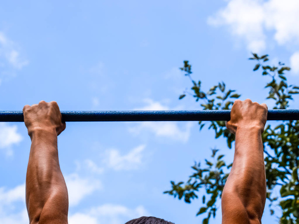 Hands on the bar close-up. The man pulls himself up on the bar. Playing sports in the fresh air. Horizontal bar. - 写真・画像