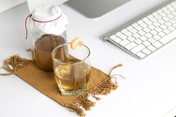 bebida fermentada, chá jun probiótico natural saudável em um frasco de vidro, com um copo e tangerina pronto para beber no escritório
 - Foto, Imagem