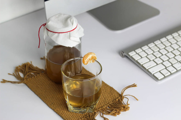 fermente içecek, bir cam kavanozda jun çay sağlıklı doğal probiyotik, bir bardak ve mandalina ofiste içmeye hazır - Fotoğraf, Görsel