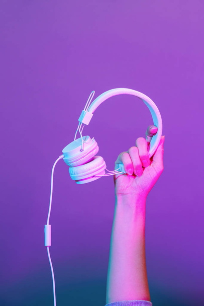 Hands with white headphones on violet background. - Photo, Image