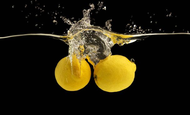 Ripe yellow lemons falling into water with splash - Fotografie, Obrázek