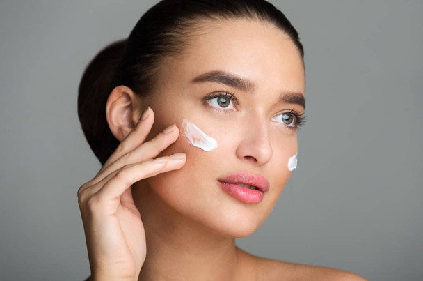 Beautiful Woman Applying Face Cream and Looking Away - Фото, изображение